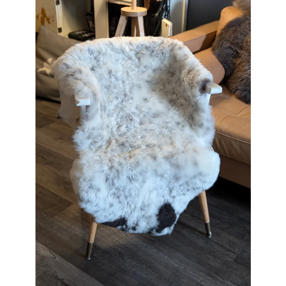 A cozy large spotted icelandic sheepskin chair cover in white and gray short wool draped over a wooden armchair