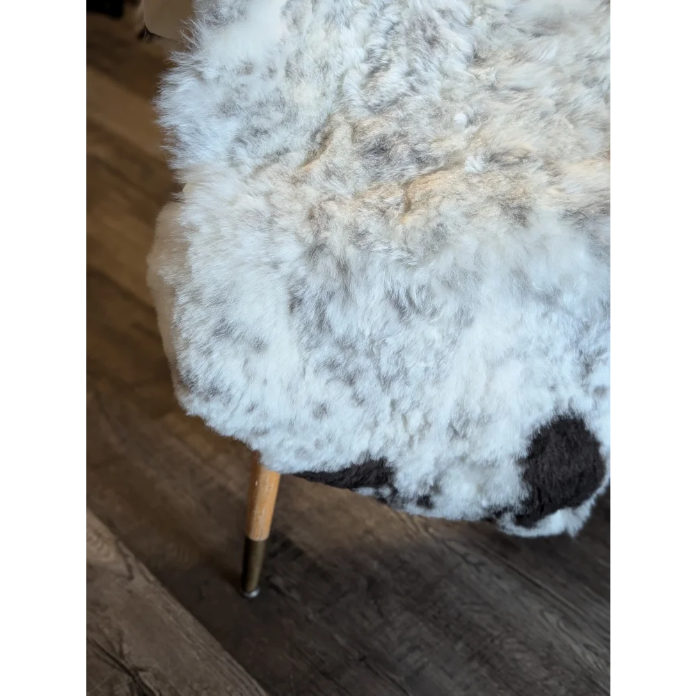 A plush white and gray faux fur ottoman with soft curly short wool and wooden legs inspired by icelandic sheepskin