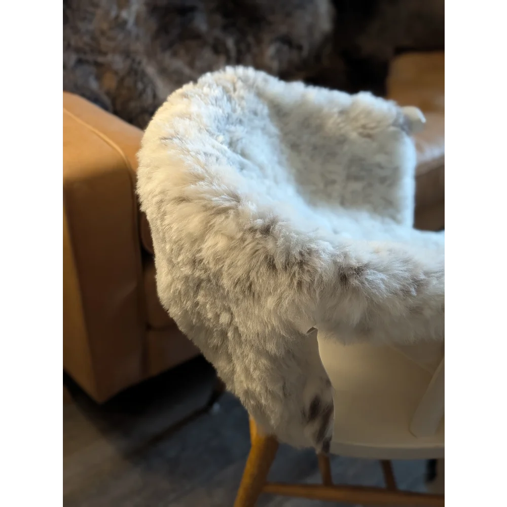 A plush white and gray spotted icelandic sheepskin throw with short wool draped over a chair for cozy use