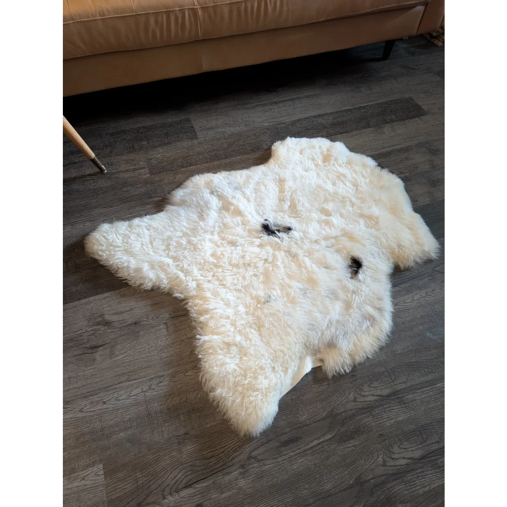A plush off-white medium icelandic sheepskin rug with short wool texture and two small black patches on the surface