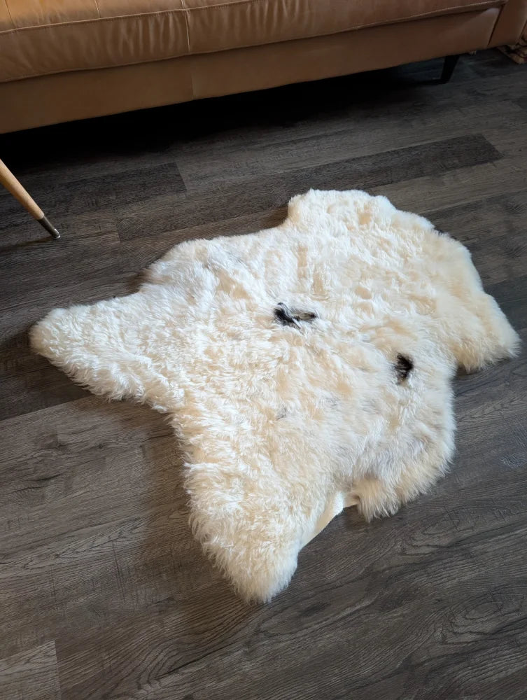 A plush off-white medium icelandic sheepskin rug with short wool texture and two small black patches on the surface