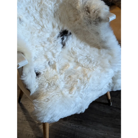 White icelandic sheepskin rug with black patches and short wool draped over the back of a wooden chair