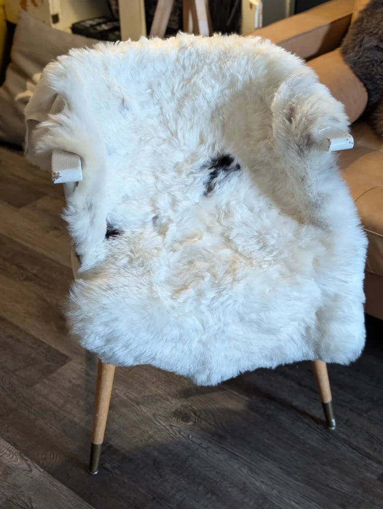 A cozy white icelandic sheepskin chair with wooden legs and metal caps featuring medium short wool spots