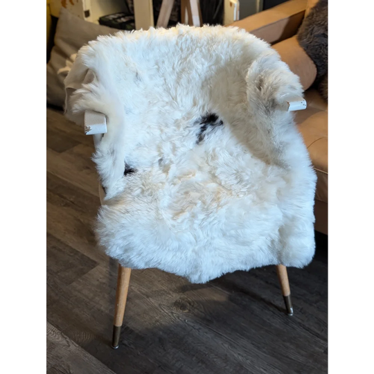 A cozy white icelandic sheepskin chair with wooden legs and metal caps featuring medium short wool spots