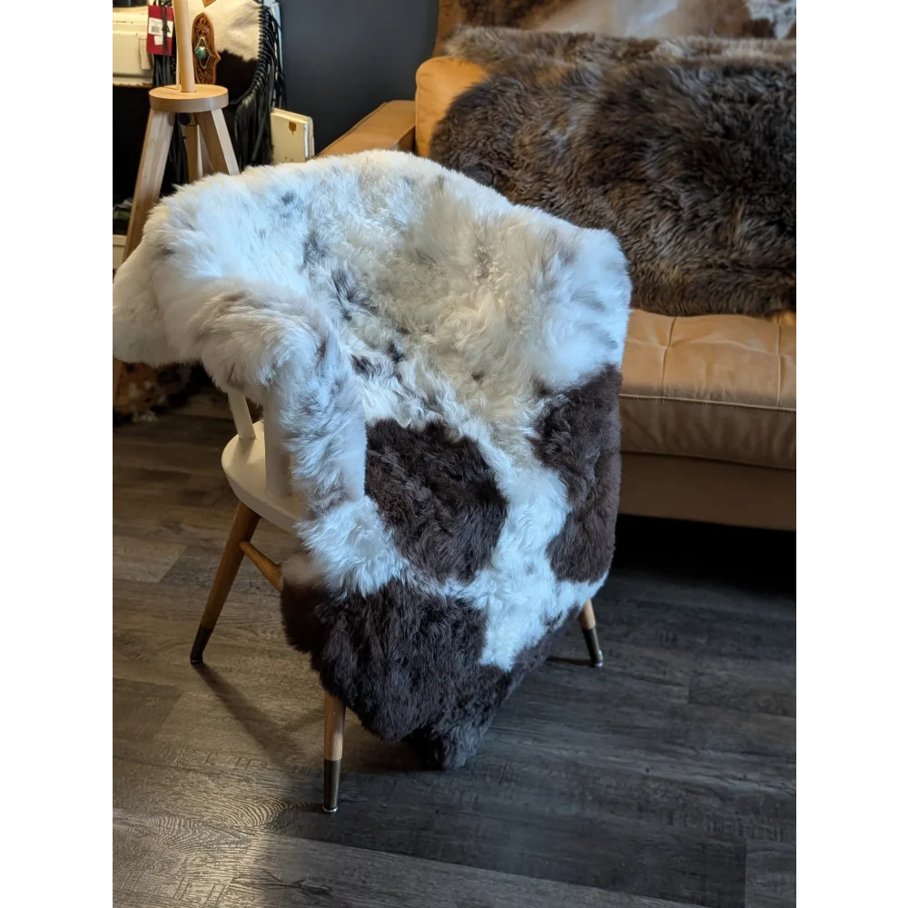 A large 48 by 37 icelandic sheepskin throw with short wool in white and dark brown patchwork draped on a wooden chair