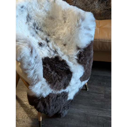 A plush icelandic sheepskin throw with white and dark brown spots made of short wool draped over an armchair back