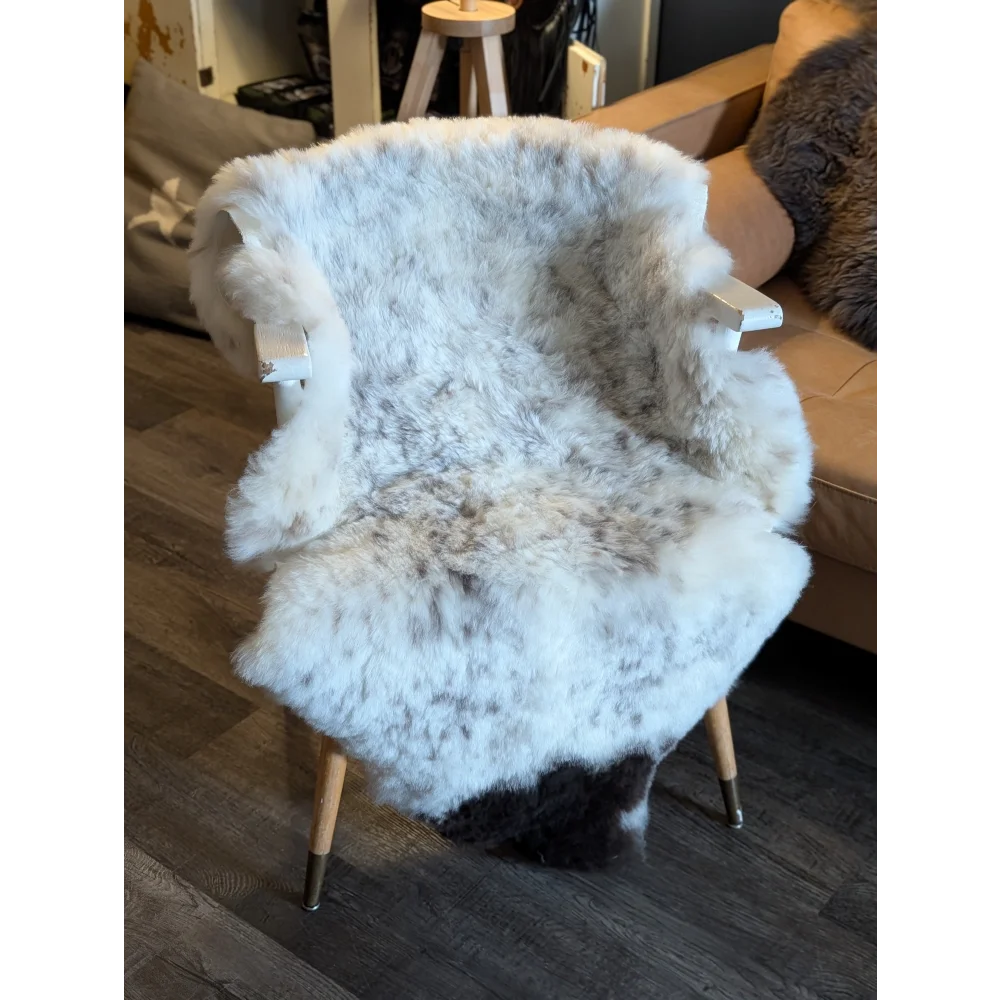 A cozy white and gray spotted icelandic sheepskin cover with short wool draped over a modern wooden armchair