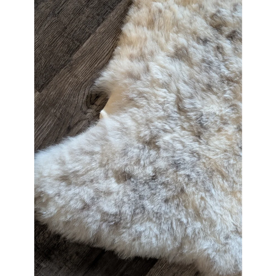 A plush icelandic sheepskin rug with short wool in soft white beige and grayish brown spotted design measuring 50 by 30.5 inches