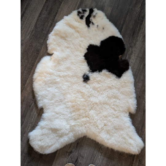 A plush cream icelandic sheepskin rug with irregular black patches and short wool texture spot 24 49 by 32 inches