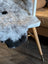 A plush gray and black icelandic sheepskin with short wool draped over a white chair with wooden legs