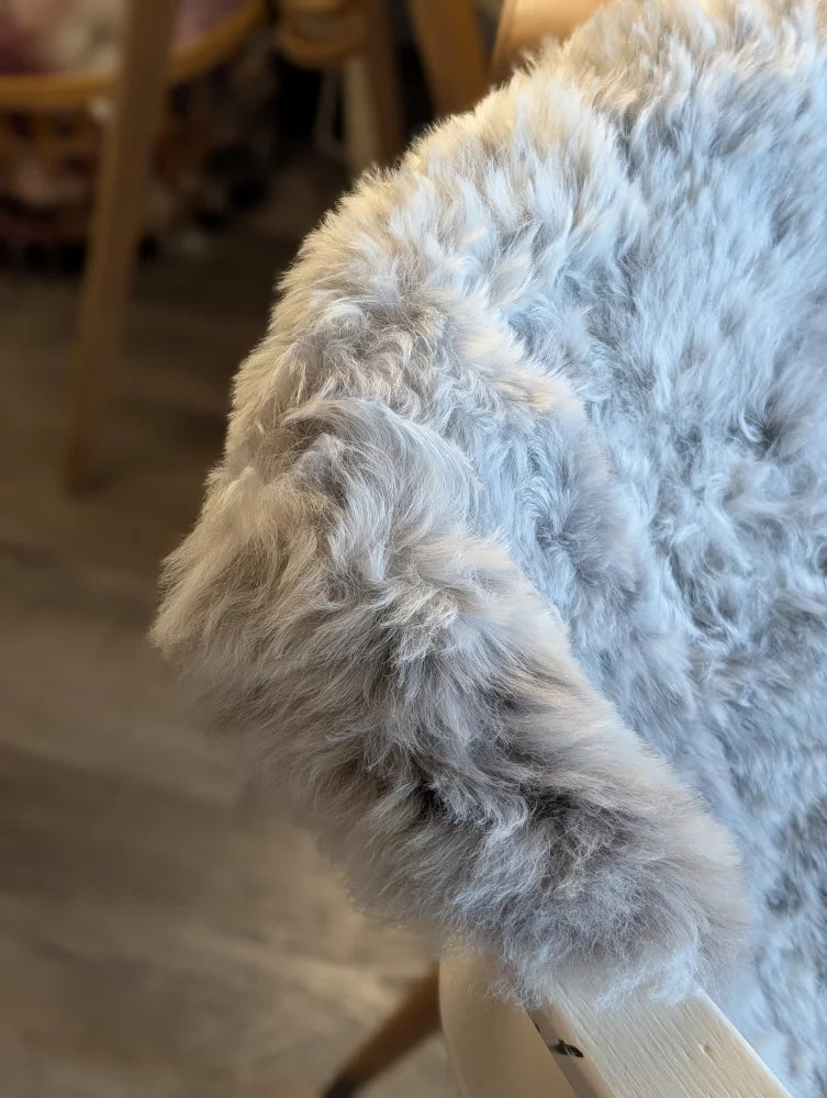 A plush light gray icelandic sheepskin throw with short wool draped over a wooden chair arm for cozy use