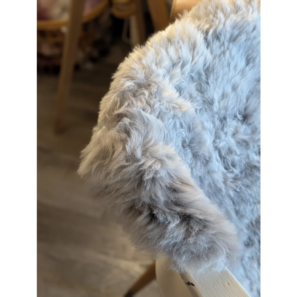 A plush light gray icelandic sheepskin throw with short wool draped over a wooden chair arm for cozy use