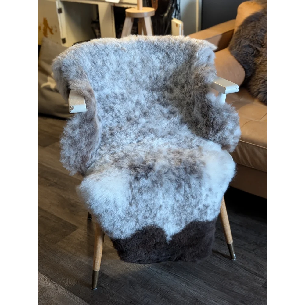 Cozy gray and white irregular icelandic sheepskin throw with soft short wool draped on wooden chair seat and backrest