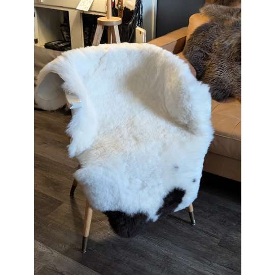 White and black spotted icelandic sheepskin short wool cover draped over a modern wooden-legged chair