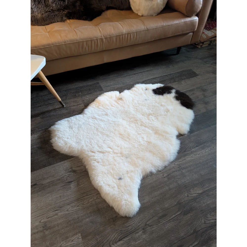White and black spotted icelandic sheepskin rug with fluffy short wool texture on dark wood flooring