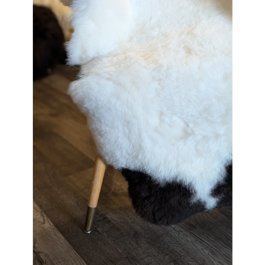 White and black icelandic sheepskin chair with wooden legs featuring large spotted short wool for cozy seating