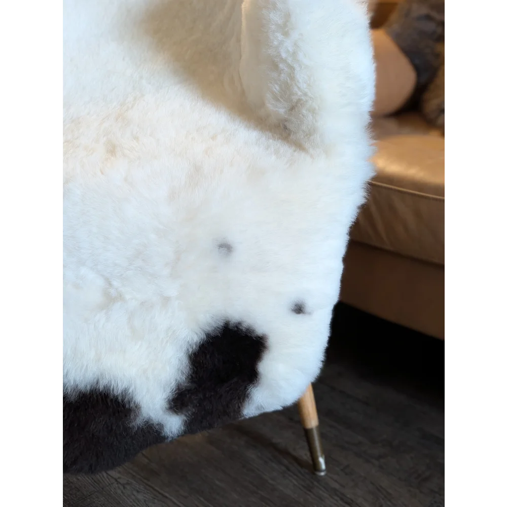 White and black cow print faux fur chair with wooden legs featuring large spotted icelandic sheepskins short wool upholstery