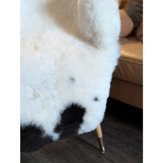 White and black cow print faux fur chair with wooden legs featuring large spotted icelandic sheepskins short wool upholstery