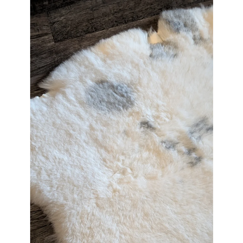 A large plush white icelandic sheepskin rug with gray spots and short wool texture measuring 47.7 by 31 inches