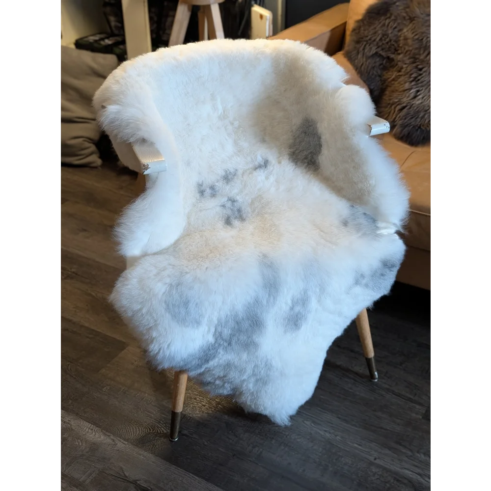 A cozy white icelandic sheepskin chair with plush short wool and light gray patches, perfect for comfy seating