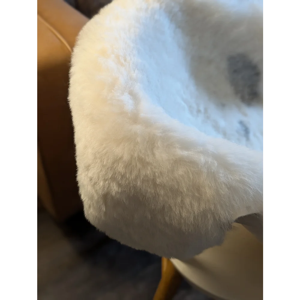 White fluffy faux fur chair cushion made from large spotted icelandic sheepskin with short wool texture