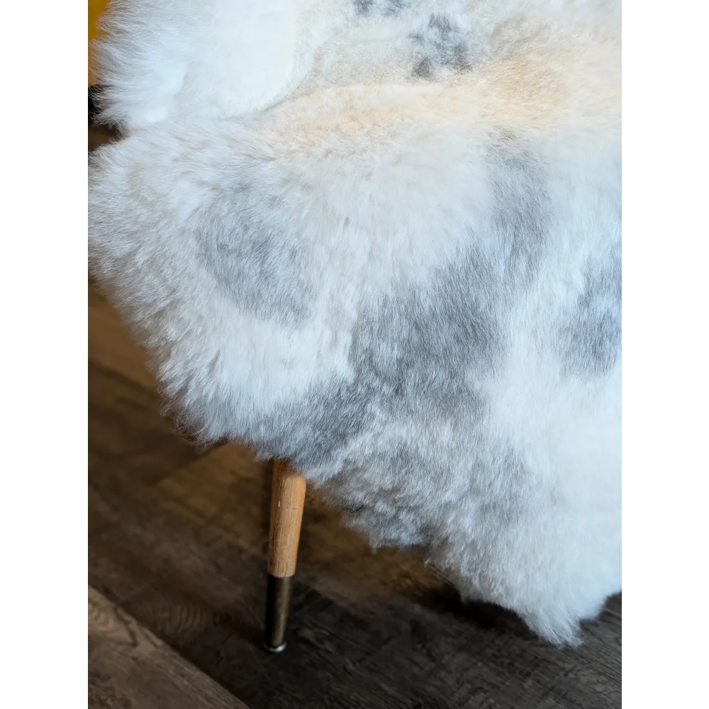 A plush white and gray icelandic sheepskin throw with soft short wool draped over a wooden-legged chair legs