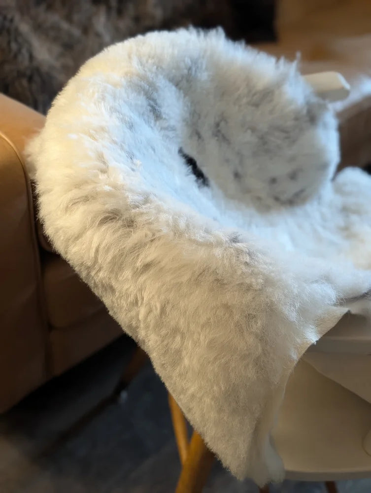 A plush white and gray icelandic sheepskin throw with short wool draped over the back of a chair