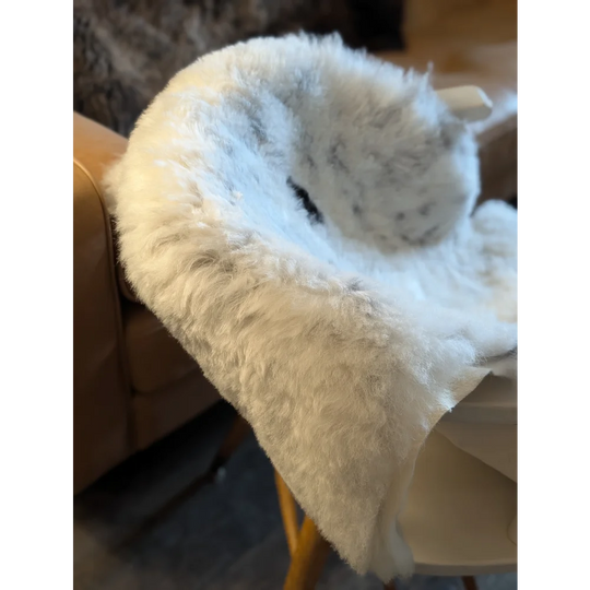 A plush white and gray icelandic sheepskin throw with short wool draped over the back of a chair