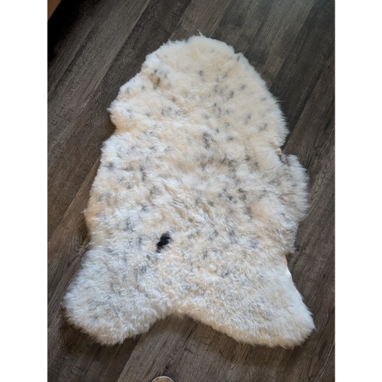 Cream-colored icelandic sheepskin rug with natural black and gray speckles made of short wool, 45 by 31 inches