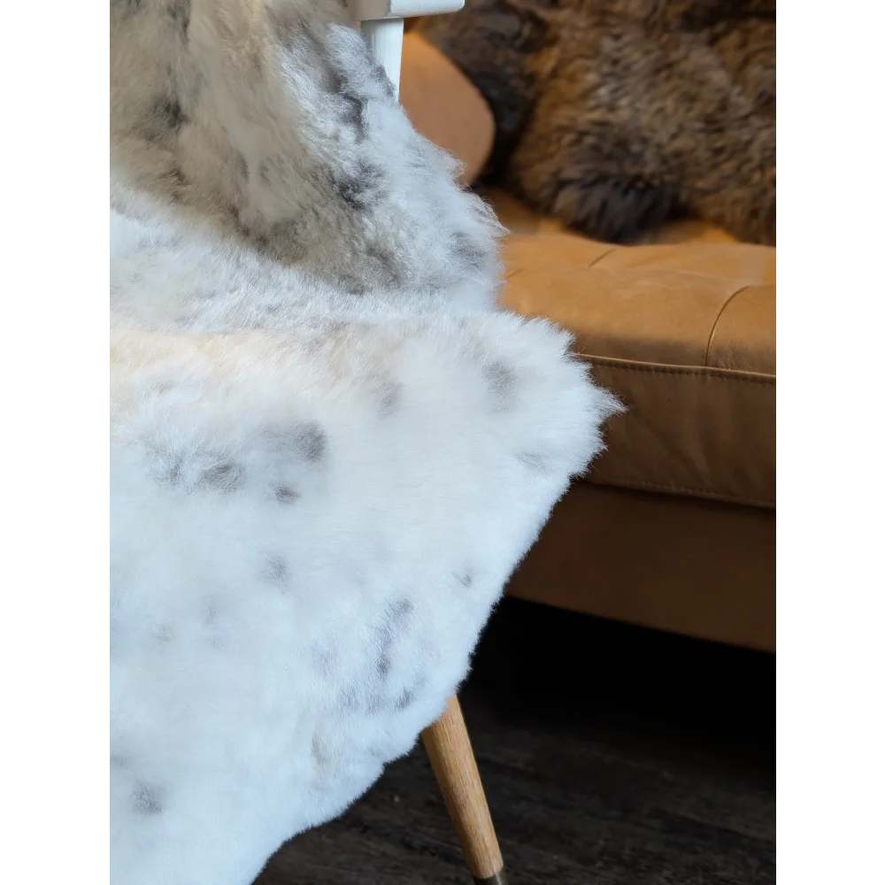 White and gray speckled faux fur throw blanket draped over chair made from short wool icelandic sheepskin