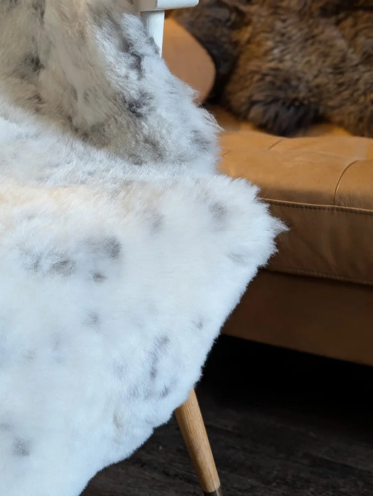 White and gray speckled faux fur throw blanket draped over chair made from short wool icelandic sheepskin
