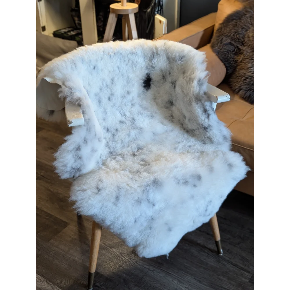 A large icelandic sheepskin throw with short wool and black speckles draped over a wooden chair