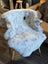 A large icelandic sheepskin throw with short wool and black speckles draped over a wooden chair