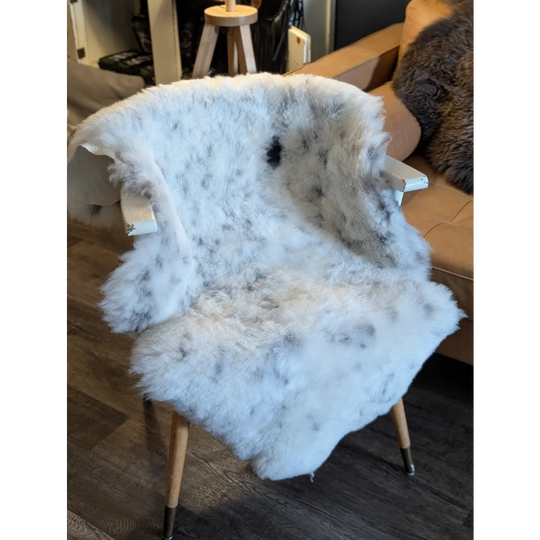 A large icelandic sheepskin throw with short wool and black speckles draped over a wooden chair