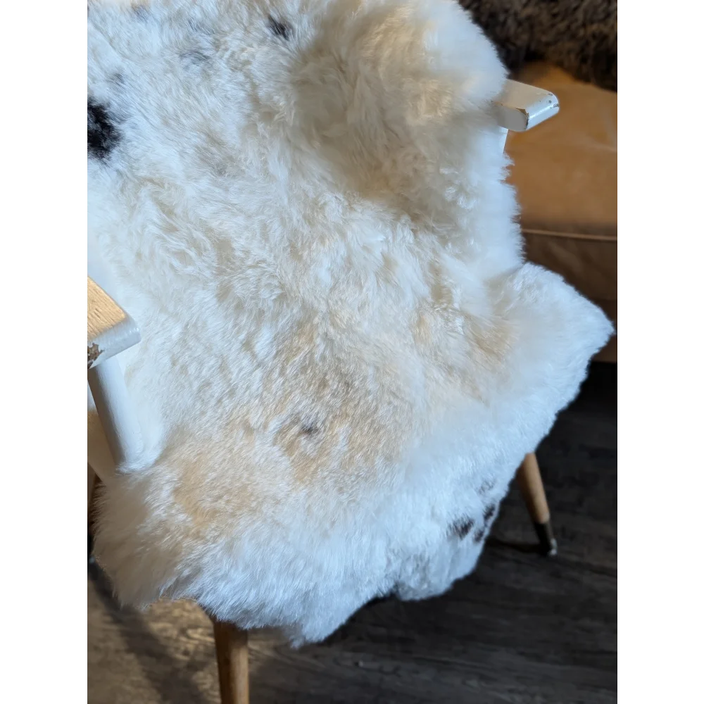 A plush white icelandic sheepskin with black spots made of short wool draped over a wooden chair