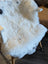 A plush white icelandic sheepskin with black spots made of short wool draped over a wooden chair