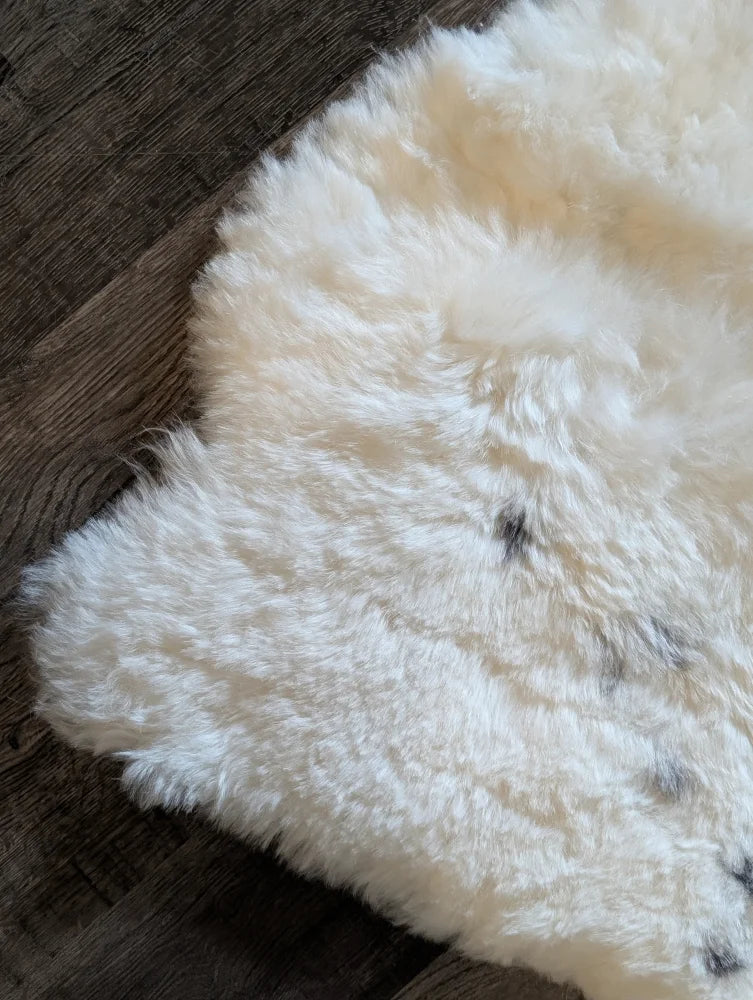 A plush off-white medium spotted icelandic sheepskin rug with soft short wool and subtle dark speckles