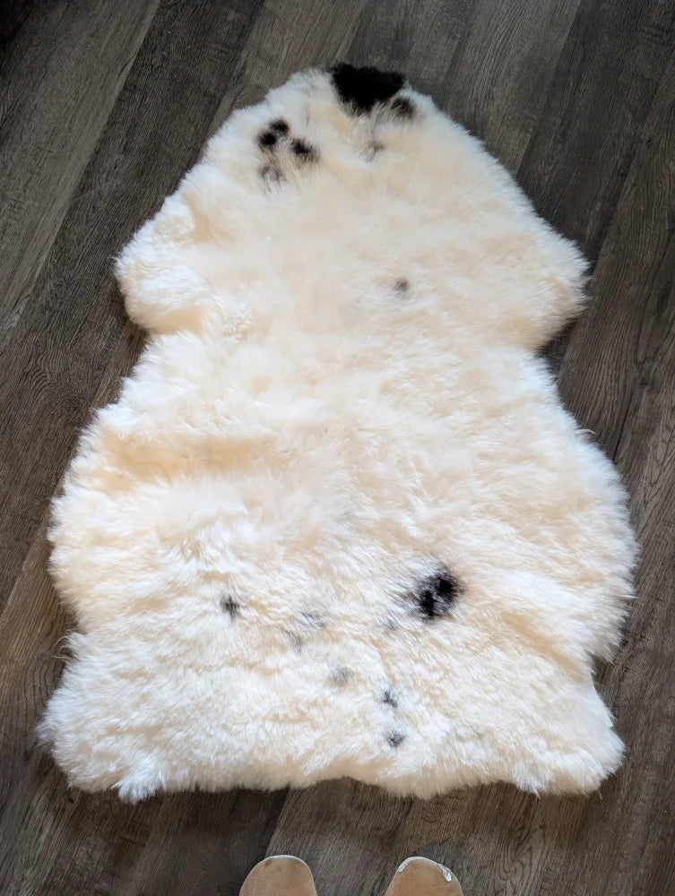 A soft cream-colored icelandic sheepskin rug with black spots made of short wool lying flat on a wooden floor