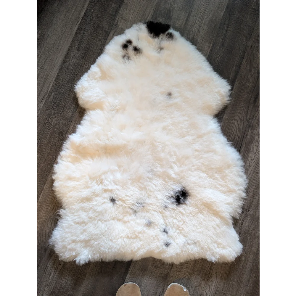 A soft cream-colored icelandic sheepskin rug with black spots made of short wool lying flat on a wooden floor