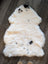 A soft cream-colored icelandic sheepskin rug with black spots made of short wool lying flat on a wooden floor