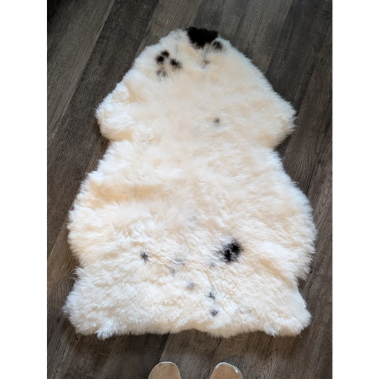 A soft cream-colored icelandic sheepskin rug with black spots made of short wool lying flat on a wooden floor