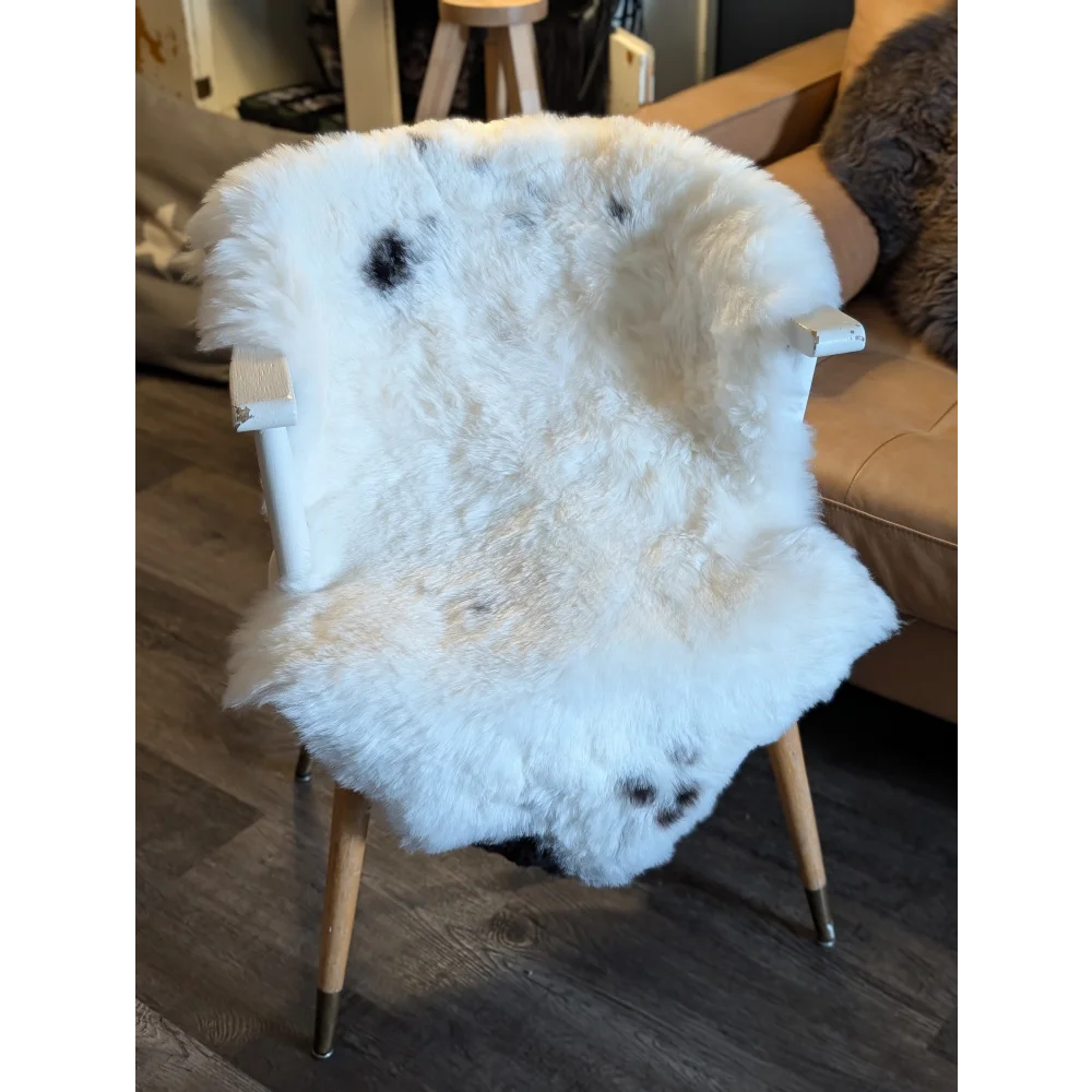 A fluffy white icelandic sheepskin chair cover with black spots made from short wool draped over a wooden armchair