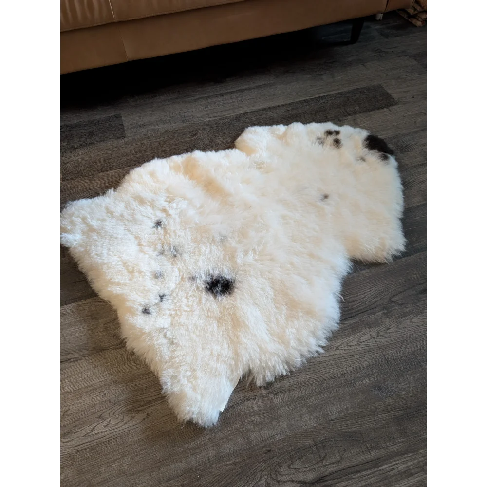Cream-colored icelandic sheepskin rug with black spot accents made of medium short wool measuring 41 by 29 inches