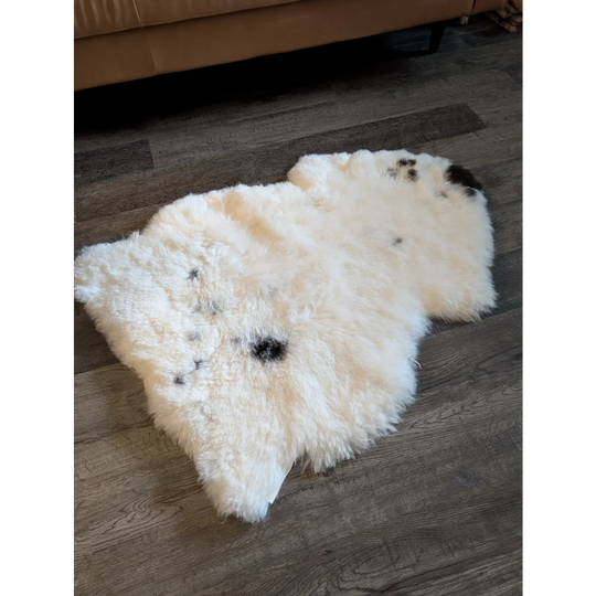 Cream-colored icelandic sheepskin rug with black spot accents made of medium short wool measuring 41 by 29 inches
