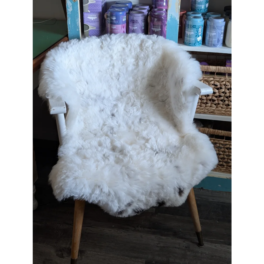 White fluffy spotted icelandic sheepskin draped over white wooden armchair with light wood legs