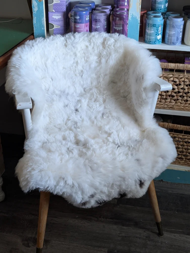 White fluffy spotted icelandic sheepskin draped over white wooden armchair with light wood legs