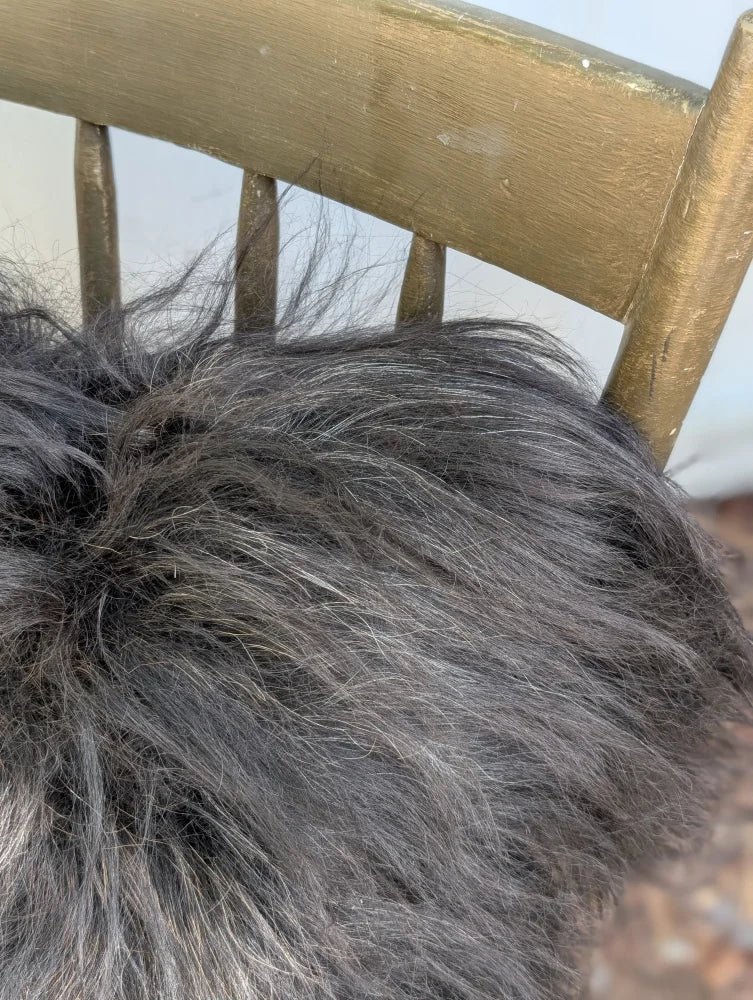 A plush dark gray icelandic sheepskin throw with long wool texture draped over a wooden chair back