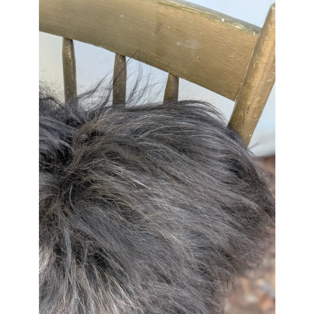 A plush dark gray icelandic sheepskin throw with long wool texture draped over a wooden chair back