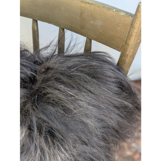 A plush dark gray icelandic sheepskin throw with long wool texture draped over a wooden chair back