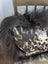 A plush black icelandic sheepskin throw with long wool draped over a cowhide pillow with white and dark brown spots